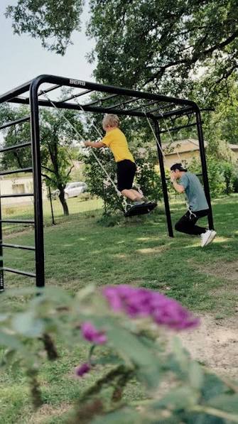 Black BERG PlayBase in a back garden with two swing seats hanging from the beam and a ladder end frame
