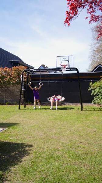 Black BERG PlayBase in a garden fitted with gym rings, a round nest swing and a basketball hoop