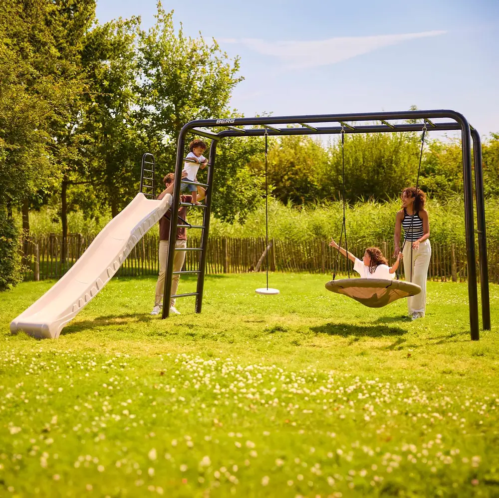 Children playing on a BERG PlayBase climbing frame with slide and nest swing